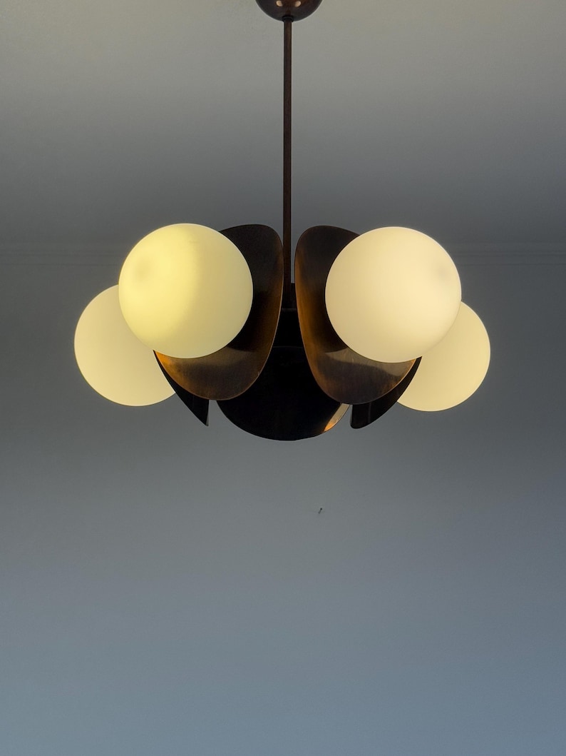 May include: A black metal chandelier with five white globe-shaped light bulbs. The chandelier has a unique design with curved arms that resemble petals.