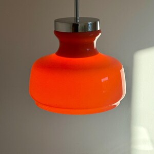 May include: Orange glass pendant light with a chrome finish. The light is hanging from a cord.