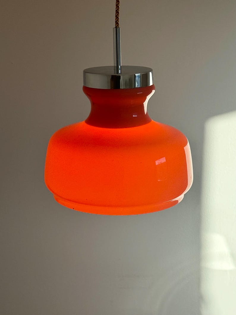 May include: Orange glass pendant light with a chrome finish. The light is hanging from a cord.
