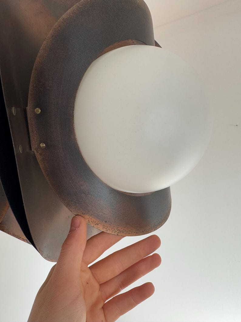 Puede incluir: Una l&aacute;mpara colgante de metal marr&oacute;n con una esfera de vidrio blanco. La l&aacute;mpara tiene un aspecto r&uacute;stico y envejecido.