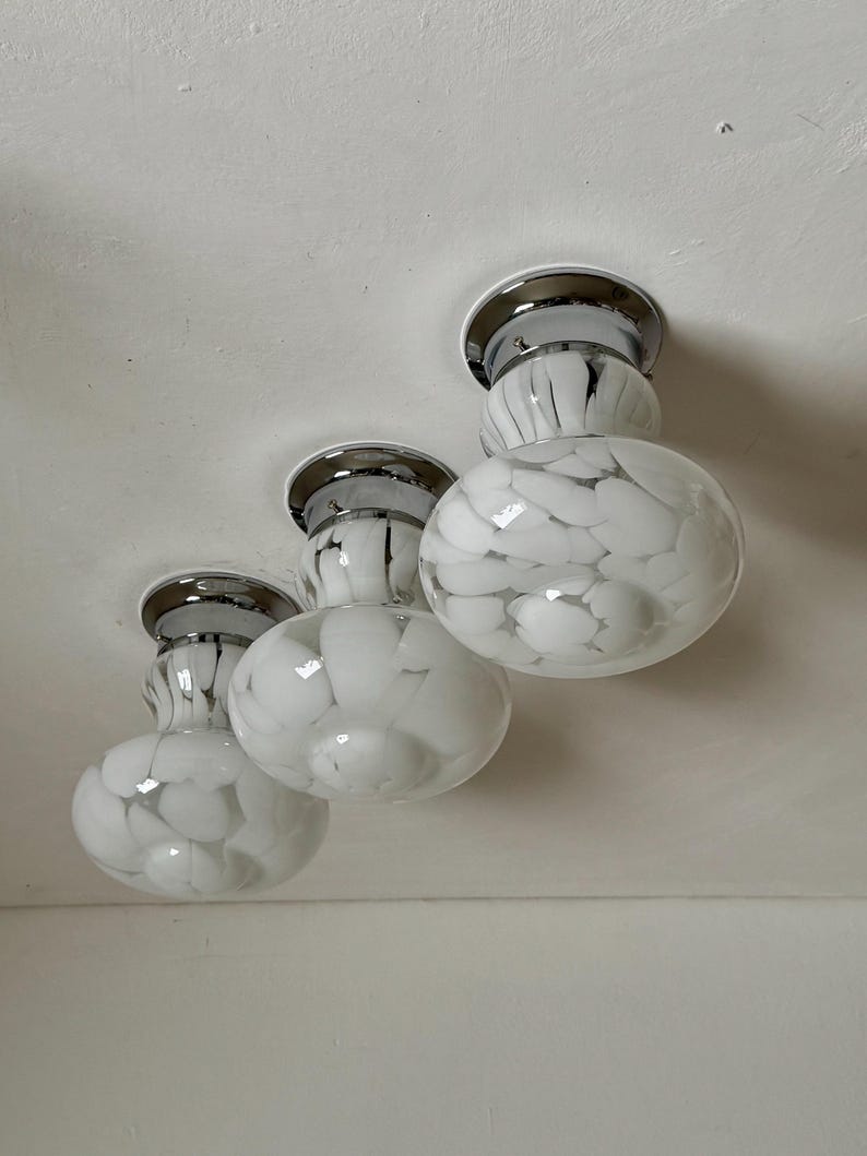 May include: Three flush-mount ceiling lights with chrome bases and white glass globes. The globes have a speckled pattern of white and black. The lights are mounted on a white ceiling.