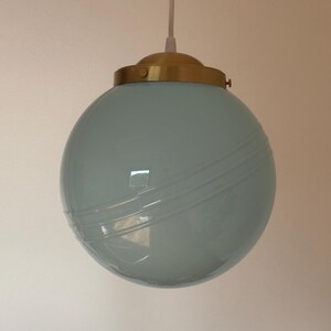 May include: A light blue glass pendant light with a gold metal fixture. The light has a round shape with a textured surface.