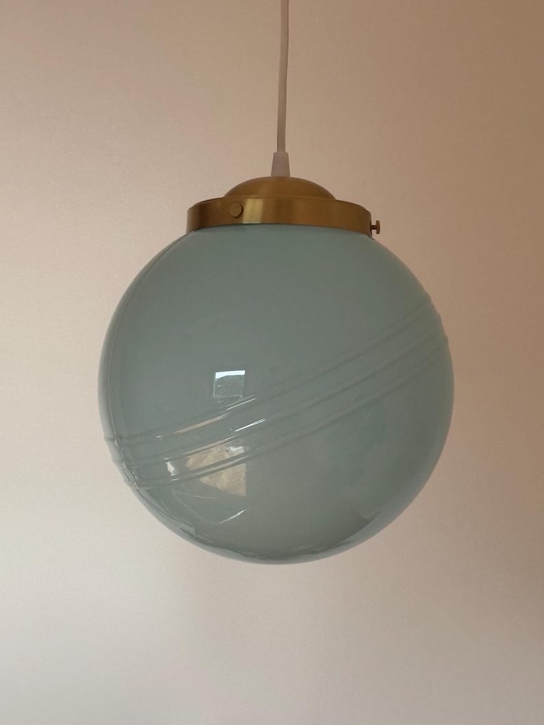 May include: A light blue glass pendant light with a gold metal fixture. The light has a round shape with a textured surface.