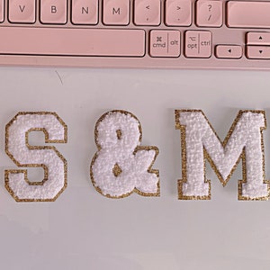 May include: White felt letters spelling "MRS & MR" with gold glitter trim. The letters are on a white surface.