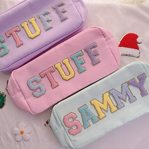 May include: Three pastel colored zippered pouches with the words "STUFF" and "SAMMY" embroidered in colorful letters.