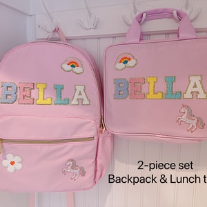 Pu&ograve; includere: Un set rosa composto da zaino e borsa per il pranzo. Lo zaino e la borsa presentano il nome "BELLA" in lettere colorate, una toppa arcobaleno, un fiore e un unicorno. Il set &egrave; progettato per bambini.