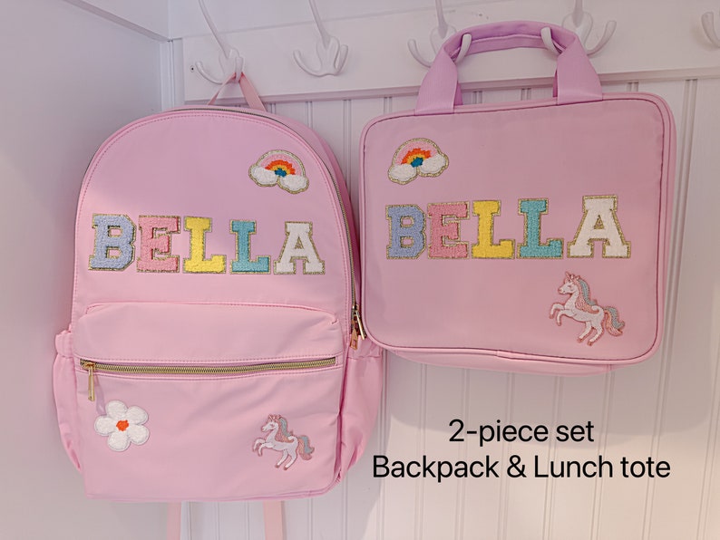 Pu&ograve; includere: Un set rosa composto da zaino e borsa per il pranzo. Lo zaino e la borsa presentano il nome "BELLA" in lettere colorate, una toppa arcobaleno, un fiore e un unicorno. Il set &egrave; progettato per bambini.