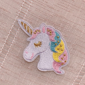 May include: A white embroidered unicorn patch with pink, yellow, and blue details. The unicorn has a gold horn and a closed eye.