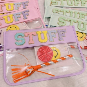 May include: A collection of clear zippered pouches with the word "STUFF" in colorful, textured letters. The pouches are in various pastel colors, and some contain small toys and accessories. A fun and organized storage solution.