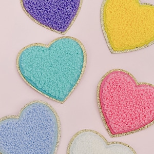 May include: Five fuzzy heart-shaped patches with gold glitter trim. The patches are in various colors: purple, yellow, turquoise, pink, and white.