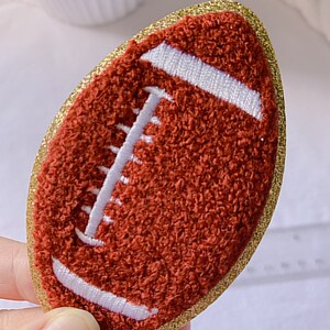 Op de afbeelding: Een bruine en witte vilt voetbal met een gouden glitterrand.