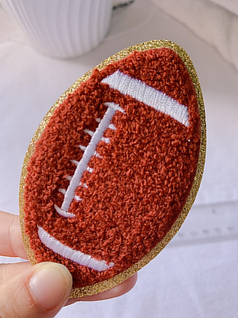 Op de afbeelding: Een bruine en witte vilt voetbal met een gouden glitterrand.