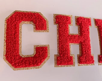 May include: Red felt letters with gold trim spelling out the word "CHI" in all caps.