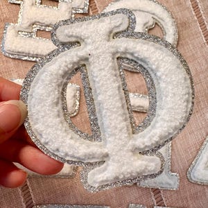May include: White felt letter with silver glitter trim. The letter is a Greek letter Phi.