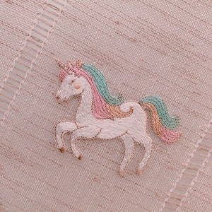 May include: A white unicorn with a pink and blue mane and tail is embroidered on a light pink fabric.
