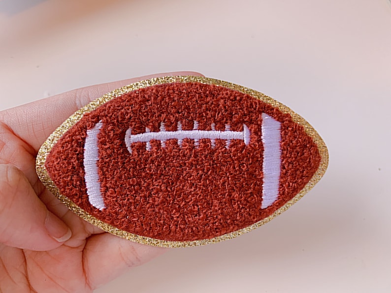 Op de afbeelding: Een geborduurde voetbalpatch in bruin en wit met een gouden glitterrand.