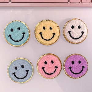 May include: Six embroidered smiley face patches with gold trim. The patches are in various colors including blue, yellow, white, pink, and purple.
