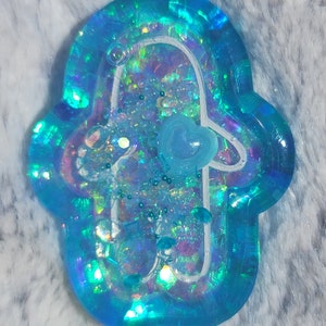 May include: A blue resin charm shaped like a hamsa hand with iridescent glitter and a blue heart charm inside.