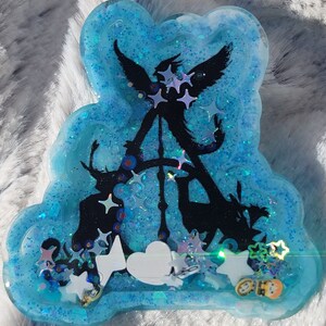 May include: A blue resin tray with a black silhouette of an angel with wings and a heart shape. The tray is filled with glitter and iridescent stars.