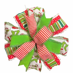 Peut inclure: Un nœud de Noël festif avec une variété de rubans. Le nœud incorpore des couleurs vertes, rouges et blanches. Certains rubans ont un imprimé du personnage du Grinch, tandis que d'autres ont des rayures et des pois. Les bords sont garnis d'un matériau vert brillant.