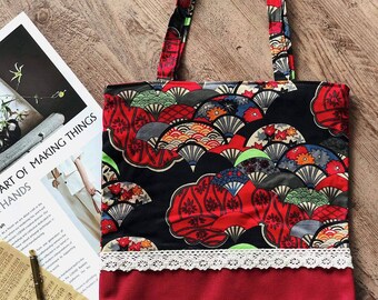 May include: A red tote bag with a black and white floral print featuring fans. The bag has a white lace trim and a red lining.