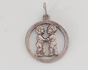 May include: Silver charm pendant featuring the astrological symbol for Gemini, two stylized figures of twins holding hands within a circular frame.