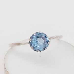Könnte beinhalten: Ein silberner Ring mit einem hellblauen Edelstein. Der Ring ist schlicht und elegant.