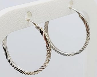 May include: A pair of silver hoop earrings with a textured, diagonal pattern. The earrings are displayed against a white background, showcasing their circular shape and intricate design. The earrings are a classic jewelry item.