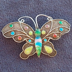 May include: A silver butterfly brooch with a wire mesh design and colorful enamel accents. The butterfly has green, blue, pink, yellow, and red enamel details.
