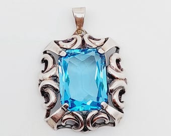 May include: A silver pendant with a large, light blue gemstone set in a decorative, ornate frame.