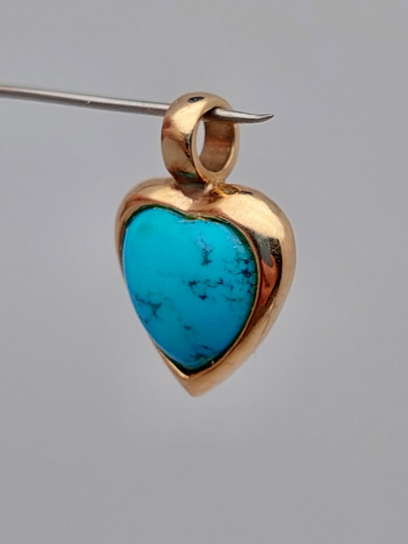 May include: A gold heart-shaped pendant with a turquoise stone set in the center.