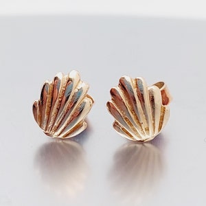May include: A pair of gold-toned seashell stud earrings. The earrings are small and delicate, with a simple design.