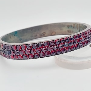 Op de afbeelding: Een zilveren armband met een rij rode granaatsteen.
