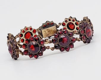 May include: A vintage garnet bracelet with a gold tone finish. The bracelet features a repeating pattern of flower-shaped clusters of red garnets.
