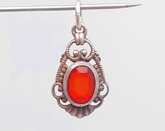 Puede incluir: Un colgante de plata con un diseño ornamentado y una piedra preciosa ovalada roja.