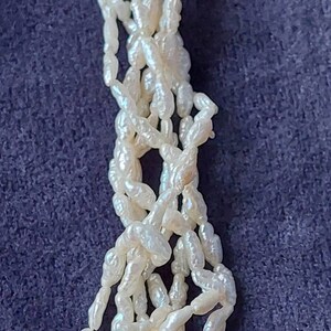 May include: A strand of white baroque pearls, with an irregular shape, strung together on a white thread. The pearls are arranged in a loose, flowing pattern.