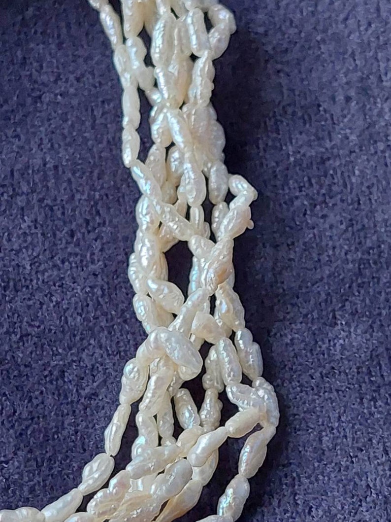 May include: A strand of white baroque pearls, with an irregular shape, strung together on a white thread. The pearls are arranged in a loose, flowing pattern.