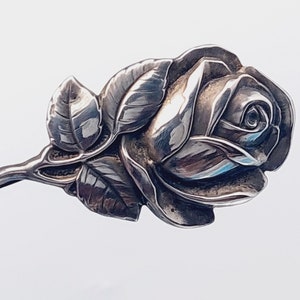 May include: A silver rose brooch with detailed leaves and a stem. The rose is a classic design and would make a beautiful gift.