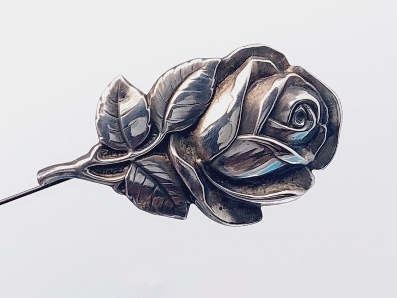 May include: A silver rose brooch with detailed leaves and a stem. The rose is a classic design and would make a beautiful gift.