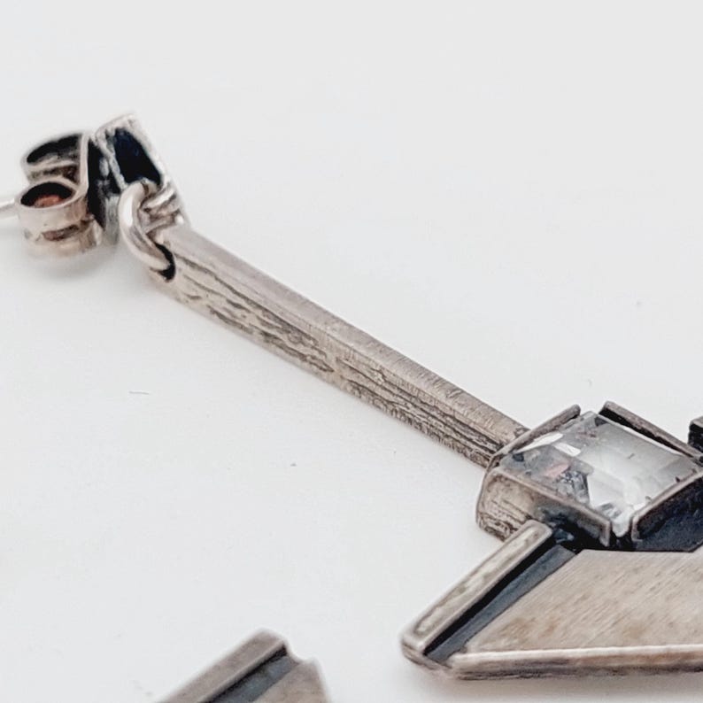 Puede incluir: Pendientes de plata con un dise&ntilde;o geom&eacute;trico y un cristal transparente. Los pendientes tienen una barra texturizada y un dise&ntilde;o puntiagudo.