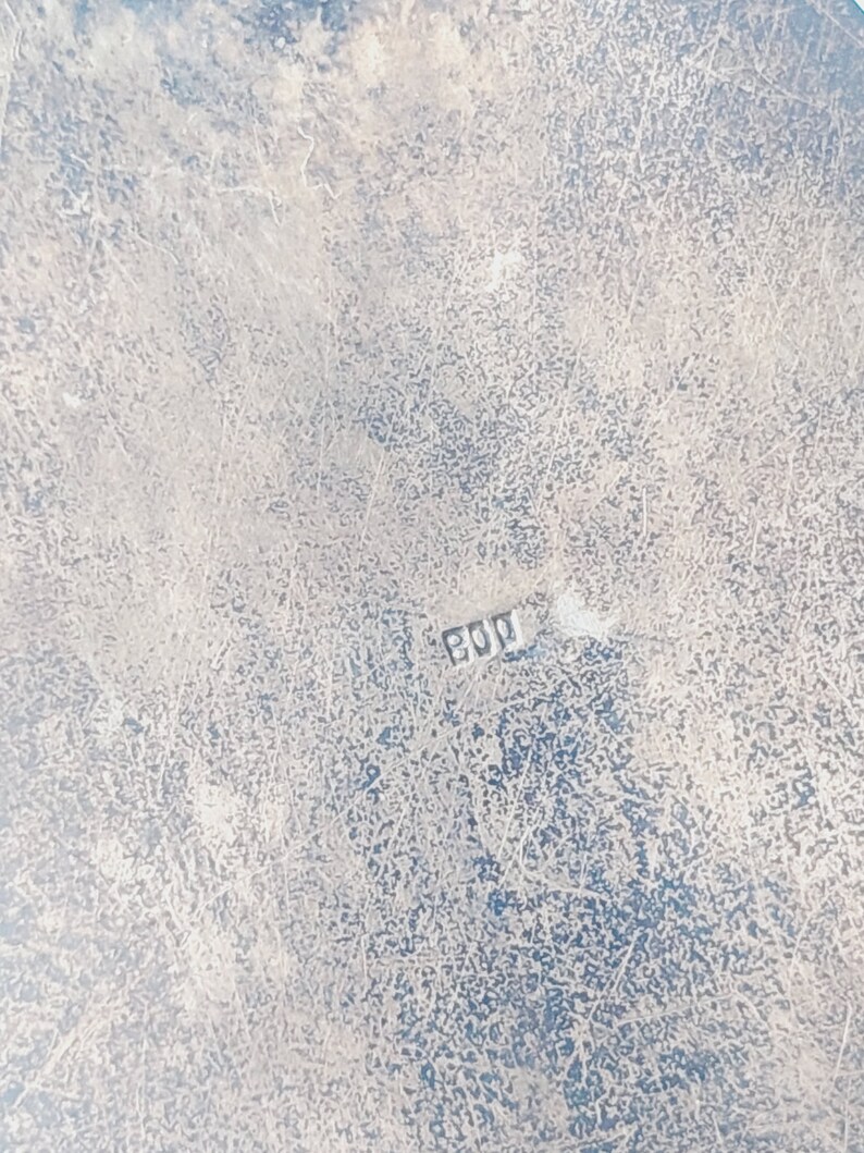 May include: Close-up of a silver-colored surface with a worn, textured finish. The surface has a faint inscription of "800" in the lower right corner.