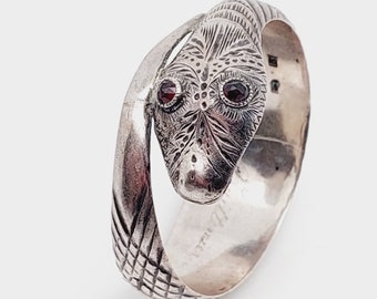 May include: A silver ring with a detailed snake design. The snake's eyes are set with red gemstones. The ring is engraved with the text "Avoral 777".