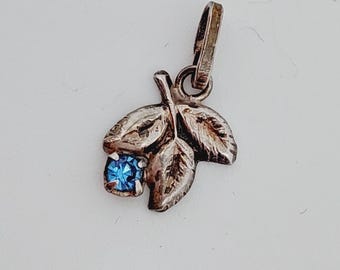 May include: A silver charm pendant featuring three leaves with a blue gemstone in the center.