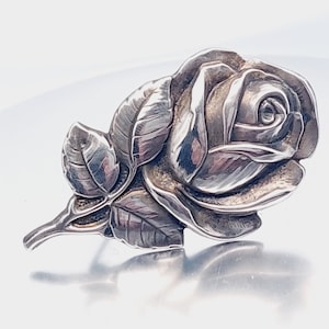 May include: A silver rose brooch with detailed petals and leaves.