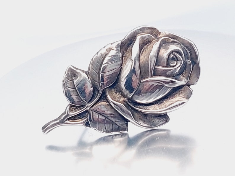 May include: A silver rose brooch with detailed petals and leaves.