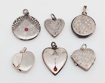 Puede incluir: Seis colgantes de plata con diseños intrincados. Los colgantes son de forma de corazón y redondos, algunos con diseños florales y otros con diseños geométricos. Cada colgante tiene un pequeño acento de piedra preciosa roja.