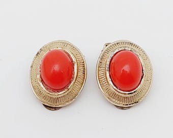 May include: A pair of vintage clip-on earrings. Each earring features a vibrant red oval stone set within a gold-toned, textured frame. The earrings have a classic, elegant design.