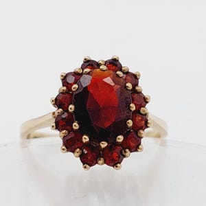 Può includere: Un anello d'oro con un grande granato rosso ovale circondato da granati rossi più piccoli.