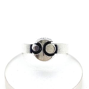 Puede incluir: Un anillo de plata con un diseño circular. El anillo presenta un círculo central texturizado con dos formas de media luna a cada lado. La banda es de diseño simple y plano. El anillo está sobre un fondo blanco.