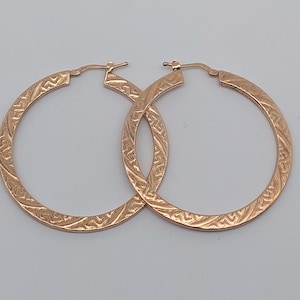 May include: A pair of gold hoop earrings with a textured design. The earrings are made of a shiny metal and have a circular shape.